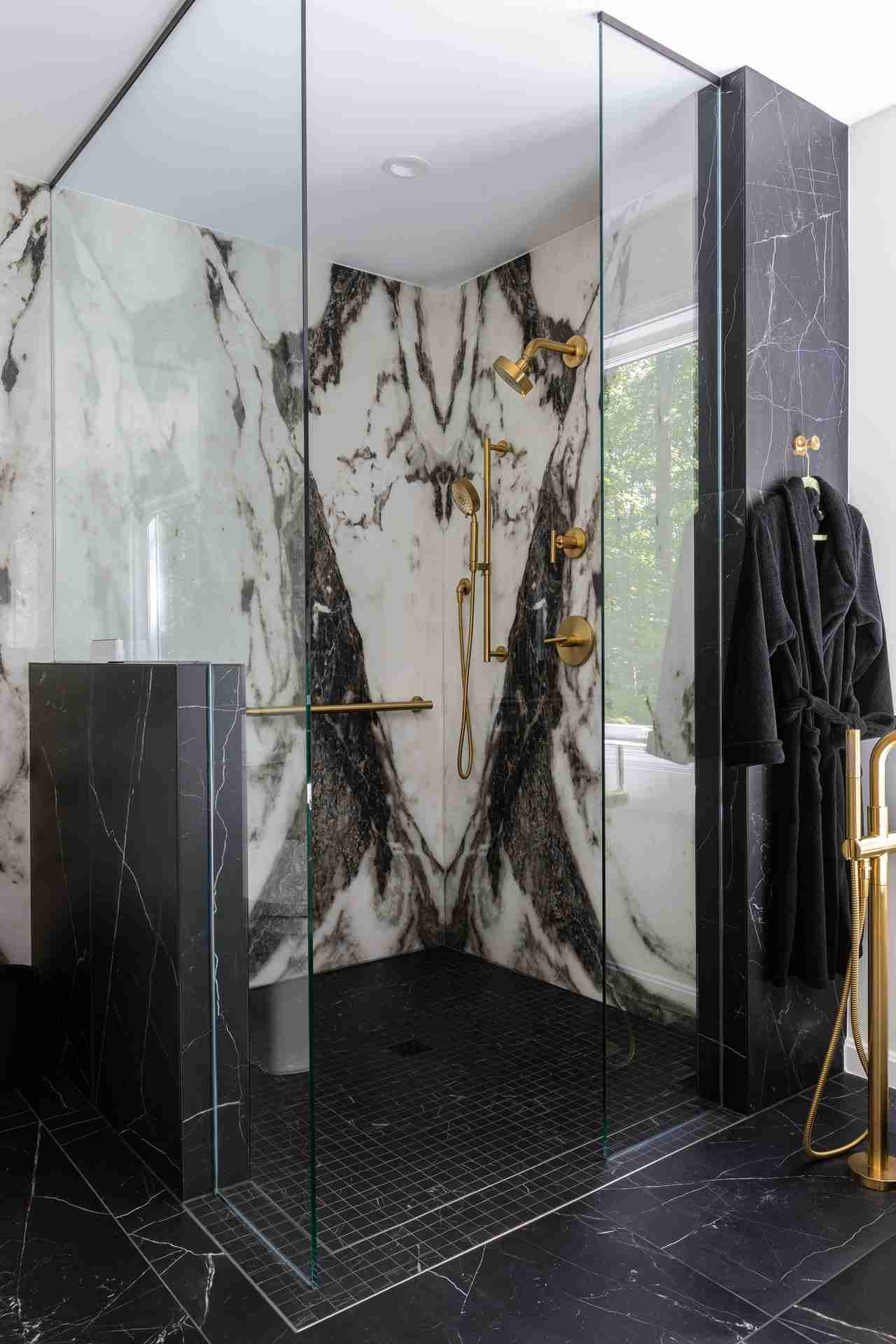 Curbless walk-in shower with a handheld fixture and marble slab walls in a Sun Design primary bathroom remodel